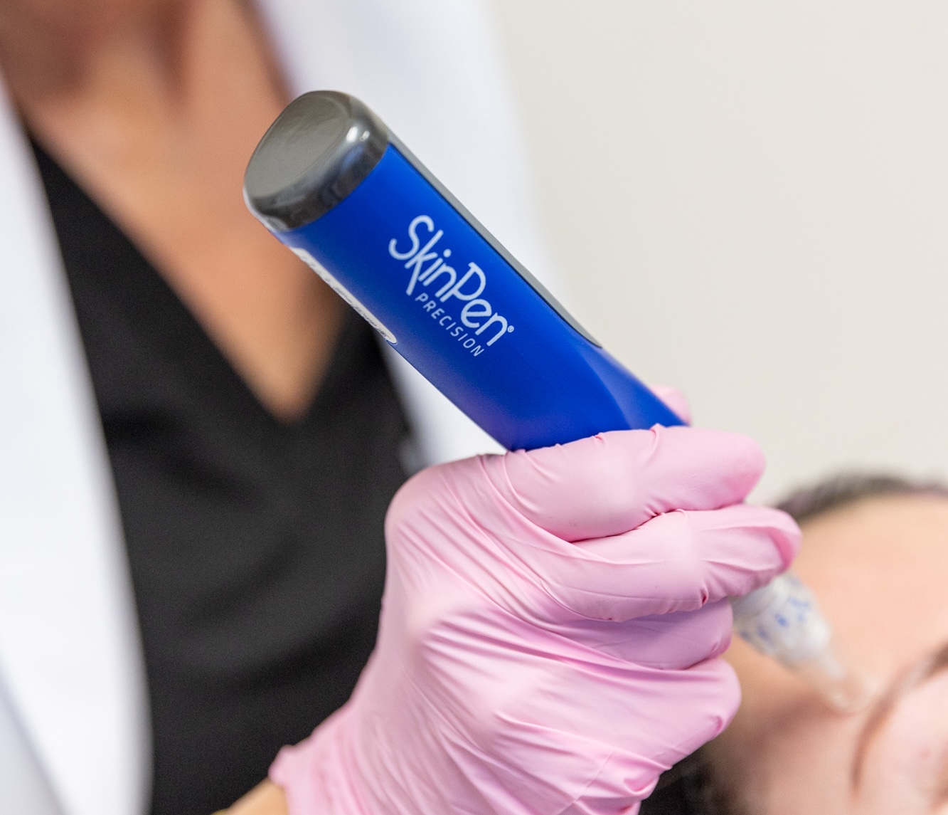 A female provider wearing pink gloves holds a SkinPen device to the forehead of a younger female patient. The patient is rejuvenating her facial skin through this approach to Atlanta microneedling.